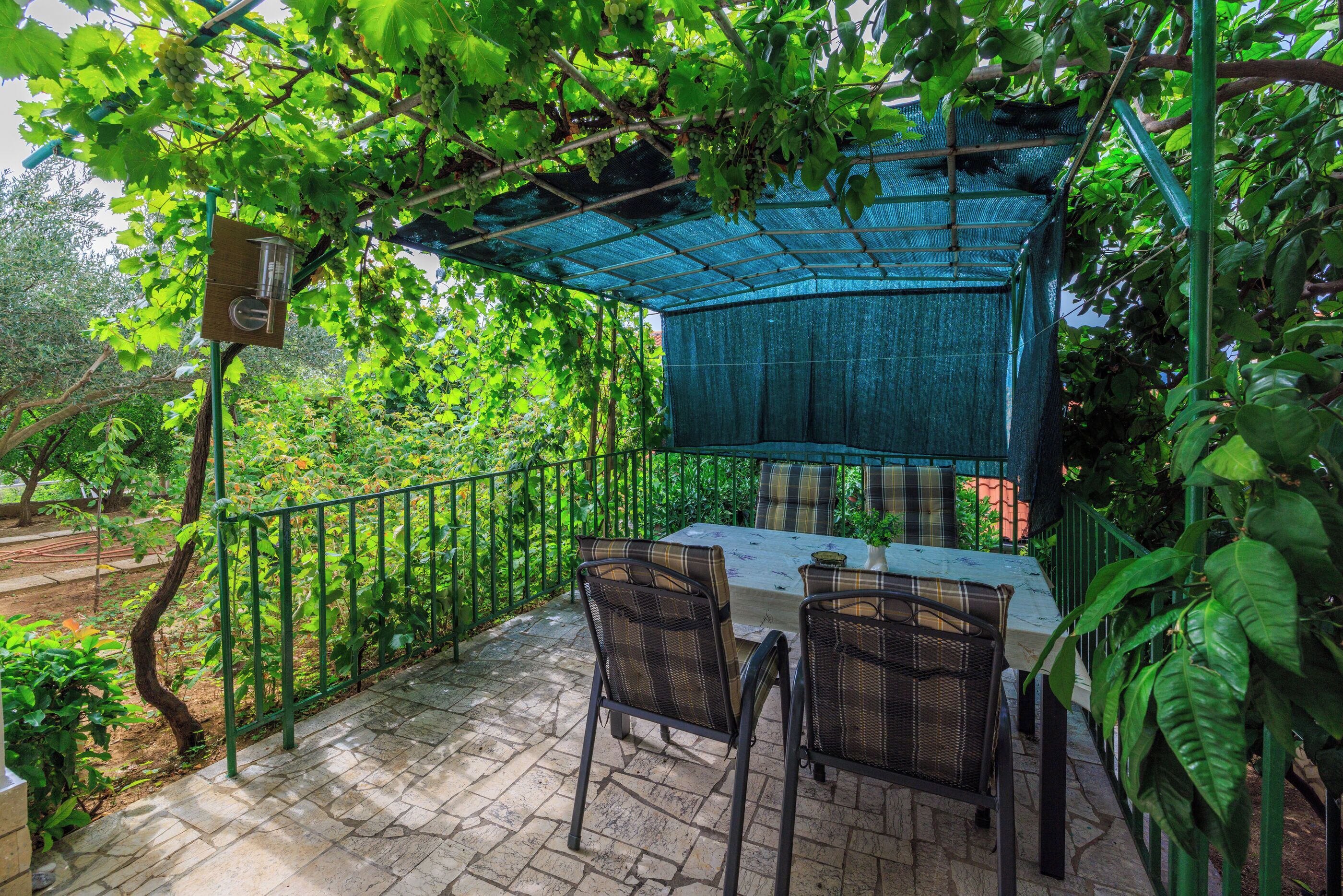 An outdoor patio with a table and chairs, surrounded by greenery and a covered area.