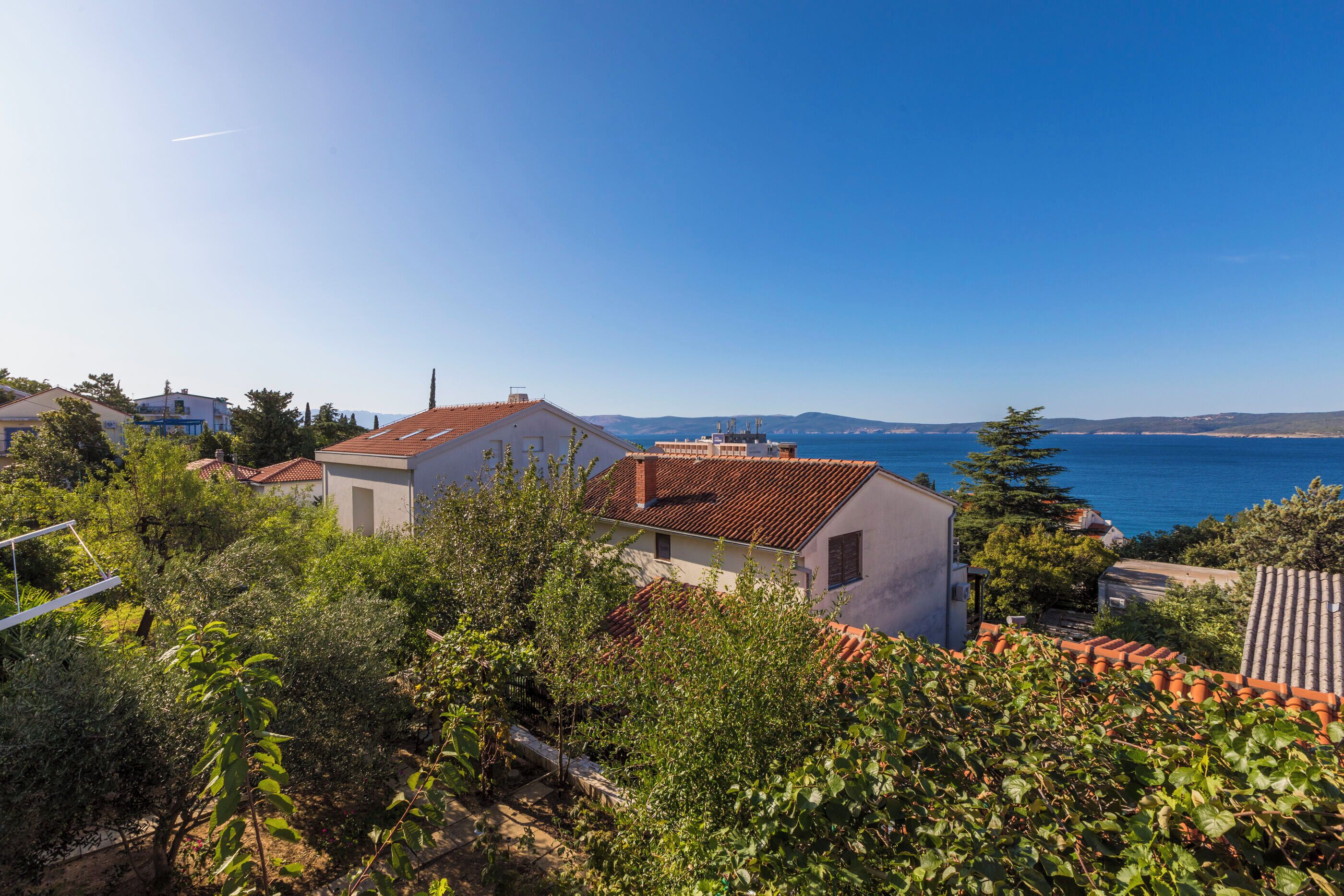 A coastal residential area with houses, greenery, and a clear view of the sea.