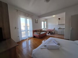 A room with a bed, a sofa, a dining table with chairs, and a kitchenette.