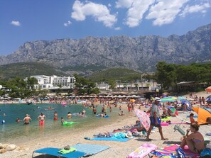 A crowded beach with people swimming and sunbathing, umbrellas, and beach chairs. - Apartments Zeljko (Makarska)
