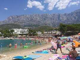 A crowded beach with people swimming and sunbathing, umbrellas, and beach chairs.