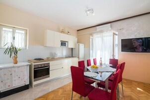 A modern kitchen with white cabinets, a microwave, and a stove. There is a dining table with red chairs and a TV mounted on the wall.