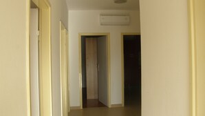 Un pasillo con unidad de aire acondicionado en el techo, una puerta de madera y suelo de baldosas.