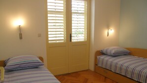 Una habitación pequeña y luminosa con dos camas individuales, suelo de madera y una puerta con persianas.