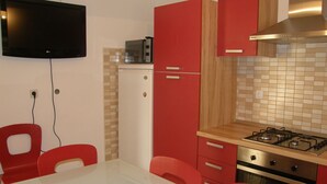 Una cocina compacta con televisor, microondas, cocina a gas y gabinetes rojos.
