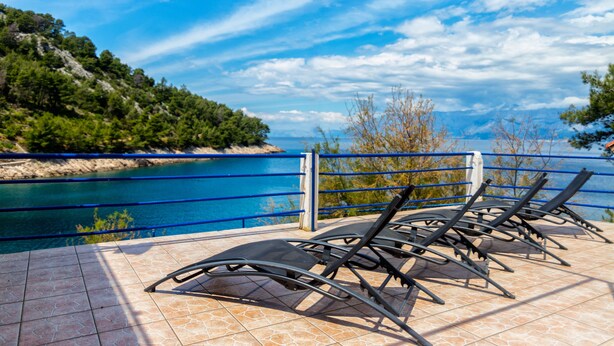 A terrace with sun loungers overlooking a body of water and a mountainous landscape. - Apartments Jelena (Sucuraj)