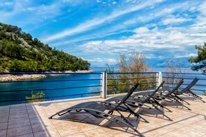 A terrace with sun loungers overlooking a body of water and a mountainous landscape. - Apartments Jelena (Sucuraj)