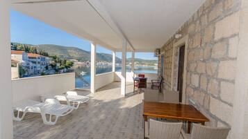 A balcony with white plastic chairs, a wooden table, wicker chairs, and a stone wall.