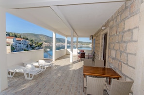A balcony with white plastic chairs, a wooden table, wicker chairs, and a stone wall. - Apartments Ivanka (Vis)