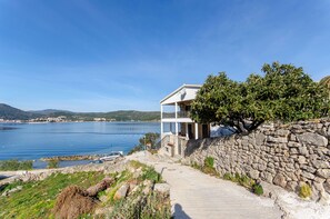 A coastal property with a stone wall, a pathway leading to a white building with a balcony, and a view of the sea. - Apartments Ivanka (Vis)