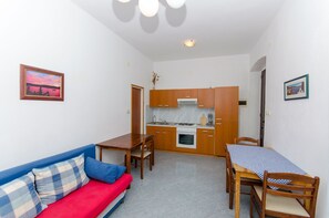 A compact living space with a kitchenette, a dining area with a table and chairs, a sofa with a red cushion, and a blue couch. - Apartments Ivanka (Vis)