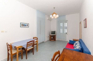 A living room with a dining table, chairs, a sofa, a TV, and curtains. - Apartments Ivanka (Vis)