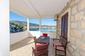 A balcony with a table and chairs, overlooking a lake and buildings. - Apartments Ivanka (Vis)