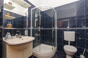 Et moderne badeværelse med en glasafskærmet brusekabine, håndvask, toilet og marmorfliser.