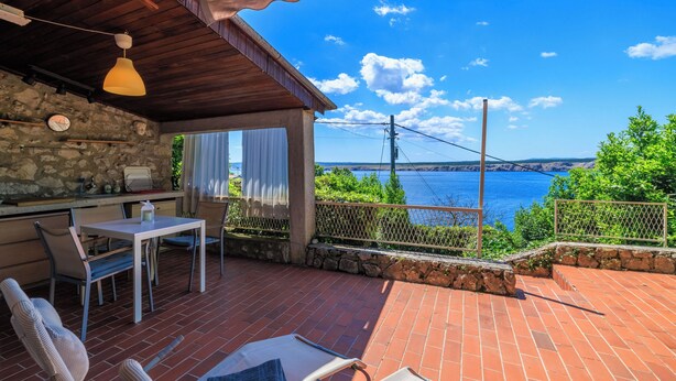 A patio with a table and chairs, a hanging light fixture, and a view of a body of water and mountains. - House Bubble (Crikvenica)