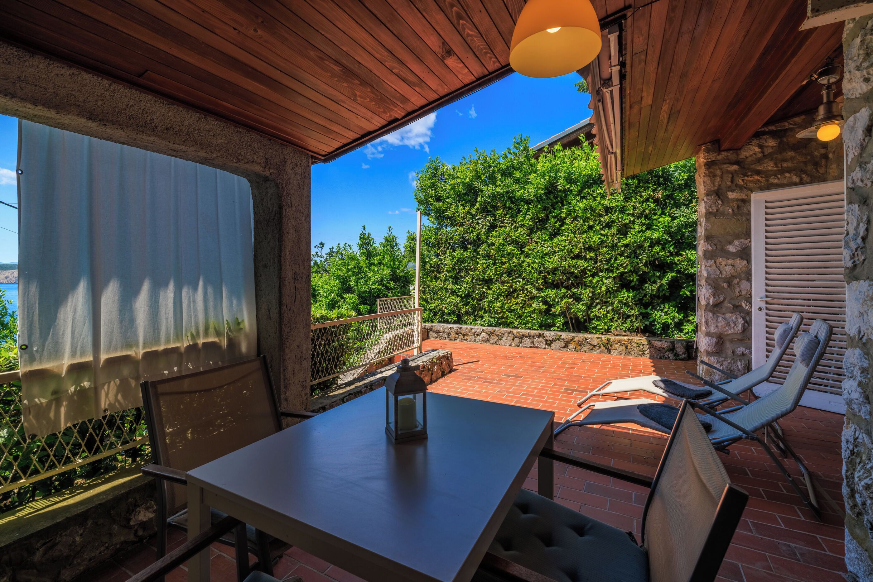 A patio with a table and chairs, a lantern, and a view of greenery.