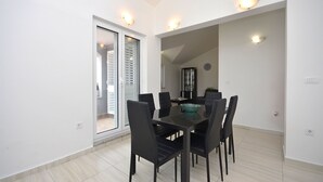 A dining area with a table and chairs, a glass door leading to a balcony, and recessed ceiling lights. - Apartment Lily With Pool Srima (Vodice)