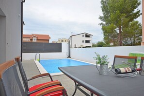 A poolside area with a table and chairs, a metal bucket, and a bottle. - Apartment Lily With Pool Srima (Vodice)