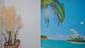 Eine Wand mit einem tropischen Strandgemälde und ein Korbwesen mit Pampasgras.