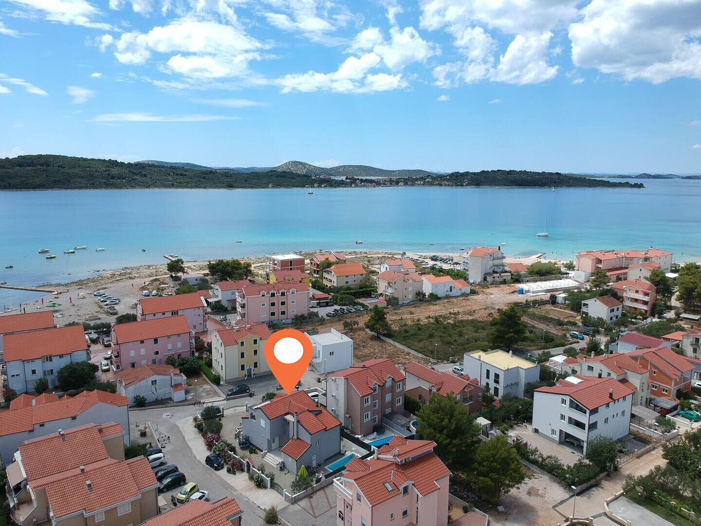 A coastal town with red-roofed buildings, a beach, and boats in the water.