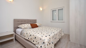 Ein Schlafzimmer mit einem Bett, einem Nachttisch, einem Fenster mit Jalousien und einer Wandleuchte.