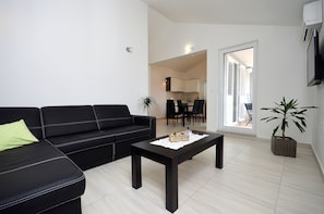 A modern living room with a black leather sofa, a wooden coffee table, and a potted plant. - Apartment Lily With Pool Srima (Vodice)