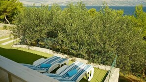 Ett poolområde med solstolar och utsikt över havet och bergen.