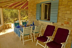 Eine Terrasse im Freien mit Esstisch und Stühlen, umgeben von einem Fenster mit blauen Fensterläden.