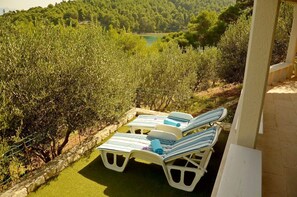 Eine Terrasse mit weißen Liegestühlen und Blick auf Olivenbäume und einen See.