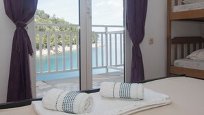 Una stanza con un letto, due asciugamani, una finestra con tende e vista su un balcone con ringhiera.
