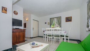 A living room with a green sofa, a white coffee table, a dining table with chairs, and a television on a wooden cabinet. - House Merica (Trogir)
