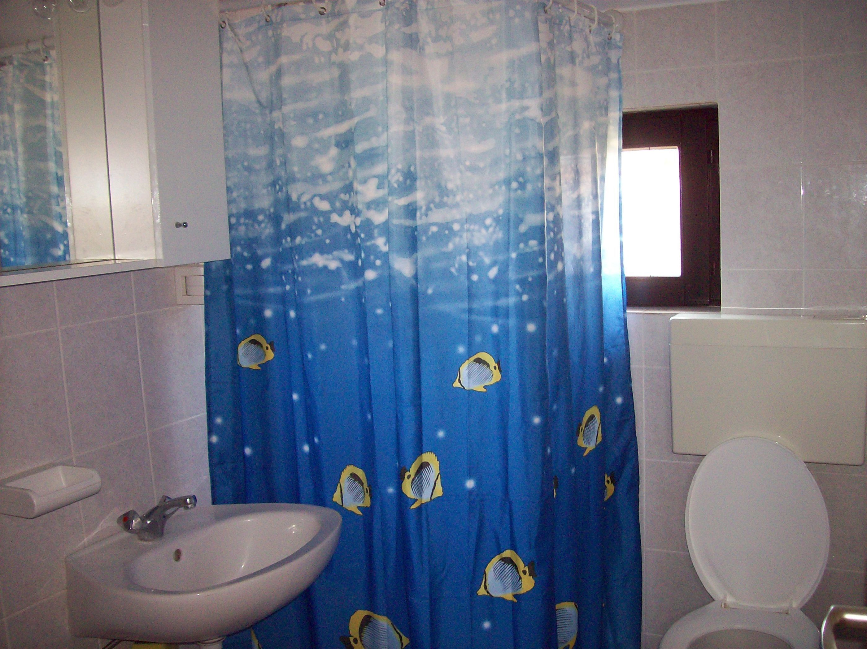 Ein Badezimmer mit blauer Duschvorhang mit Fischmuster, einem weißen Waschbecken und einer Toilette.