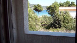 A window view of a coastal landscape with trees and a clear blue sea. - Apartments Barac (Marina)