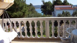 A balcony with a white balustrade, a table with a chair, and a view of the sea and trees. - Apartments Barac (Marina)