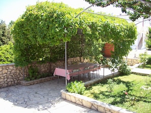 Eine Terrasse mit Tisch und Stühlen, umgeben von Grünpflanzen und einer Steinmauer.