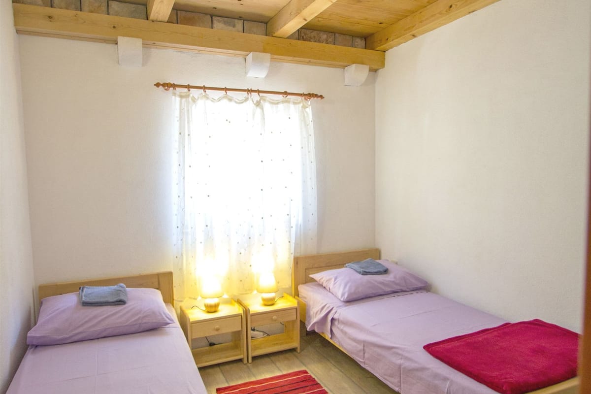 A small, cozy room with two wooden beds, a red rug, and a window with curtains.