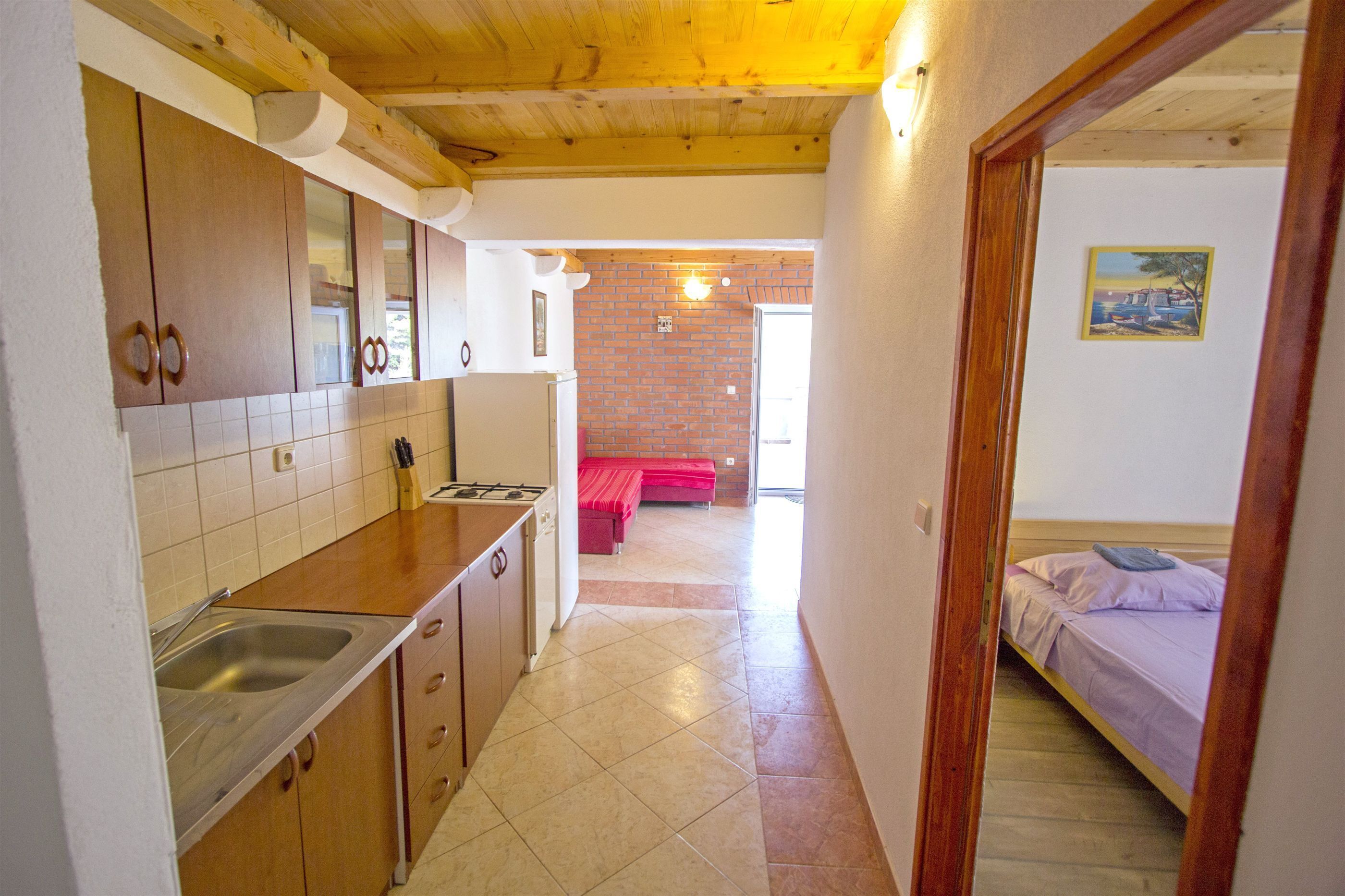 A compact kitchen with wooden cabinets, a sink, and a red bench in the background.