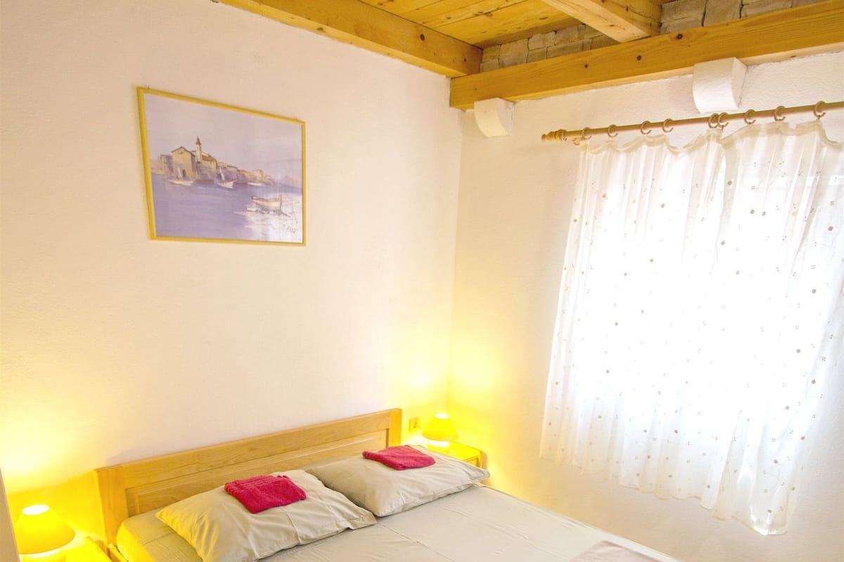 A bedroom with a wooden bed, two bedside tables with lamps, a painting on the wall, and a window with curtains.