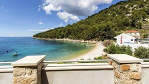 A coastal view with a clear blue sea, a sandy beach, and a white building with a red roof. - Apartments Zeljko (Jelsa)