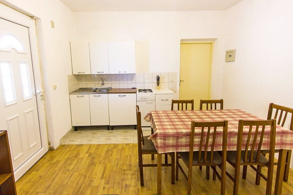 A compact kitchen with white cabinets, a small dining table with a plaid tablecloth, and wooden chairs.