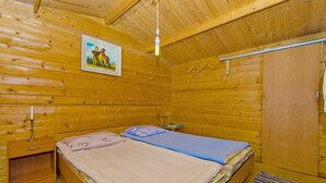 Ein Zimmer in einer Holzhütte mit zwei Betten, einem Nachttisch, einem gerahmten Bild an der Wand und einer Deckenleuchte.