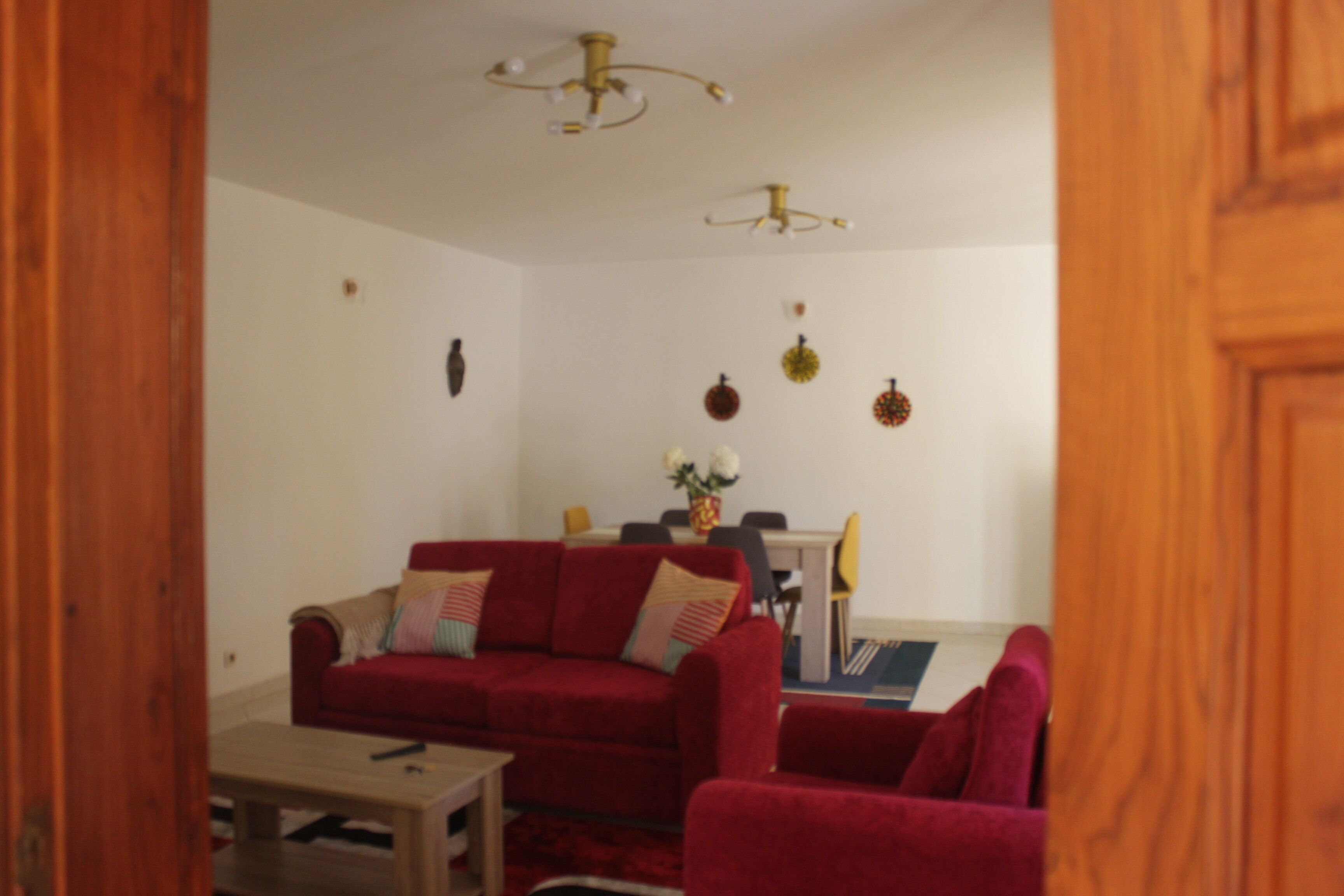 A living room with a red sofa, a small table, and a dining table with chairs. There is a ceiling light fixture above the dining table.