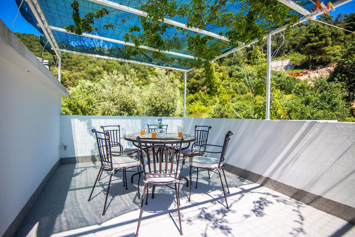An outdoor patio with a round table and six chairs, surrounded by a white wall and a metal railing.