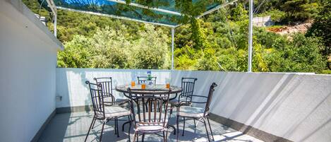 Une terrasse extérieure avec une table ronde et six chaises, entourée d’un mur blanc et d’une rambarde en métal.