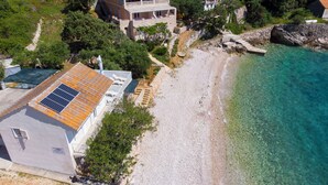 En ejendom ved kysten med et stort hus, solpaneler på taget, en strand og klart vand.