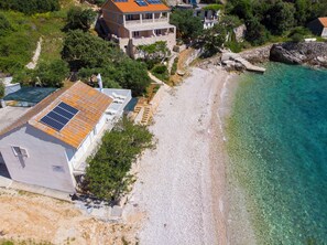 A coastal property with a large house featuring a solar panel roof, a beach, and clear waters. - Apartments Robinzon Petar (Jelsa)