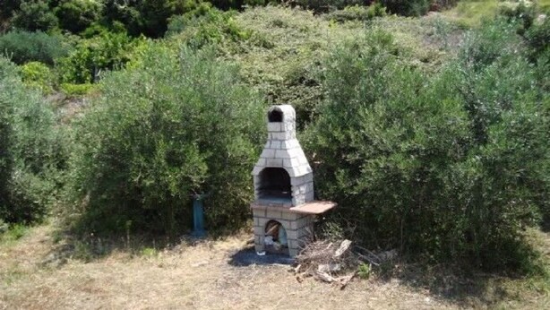 A stone-built outdoor oven surrounded by dense shrubbery. - Apartments Robinzon Petar (Jelsa)