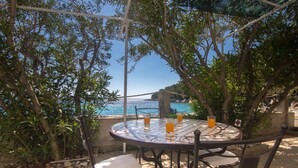 Et rundt udendørsmøbel med stole, udsigt til havet og en pergola over sig.