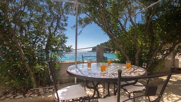 A round outdoor table with chairs, a view of the sea, and a pergola overhead.
