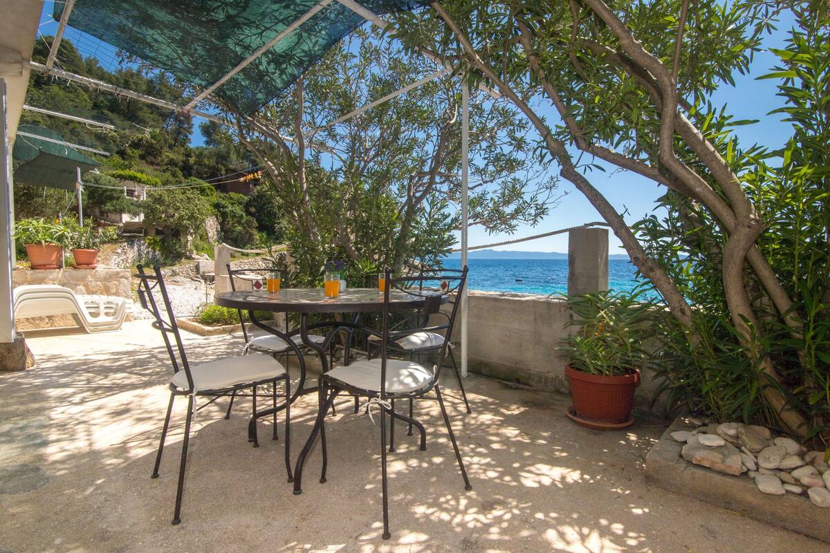 An outdoor seating area with a table and chairs, surrounded by potted plants and overlooking a body of water.